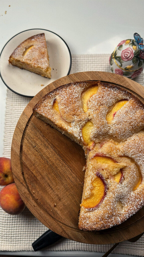Vertical overhead view of peach butter cake on a wooden board with a slice on a side plate