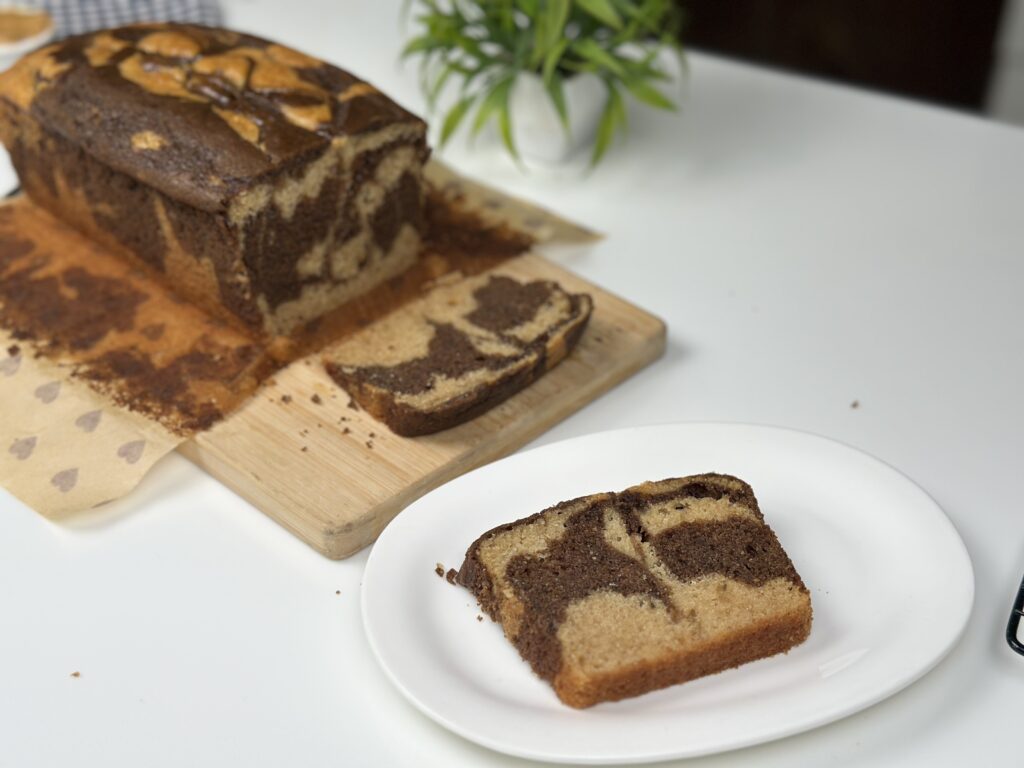 Slice of eggless marble peanut butter loaf cake served on a white plate with the loaf behind
