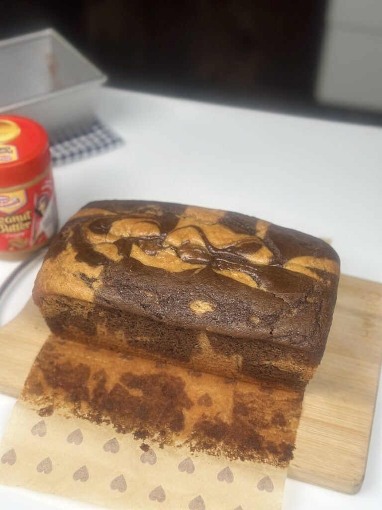 Whole eggless peanut butter marble loaf cake on a wooden board with peanut butter jar