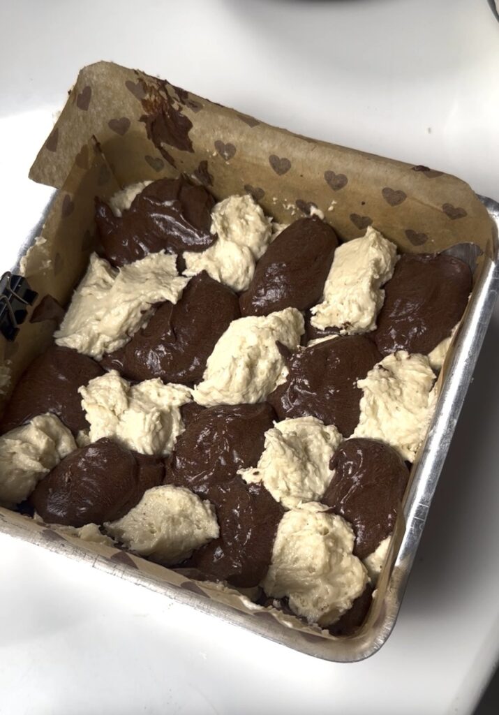 Vanilla and chocolate batter spooned into a square tin lined with parchment