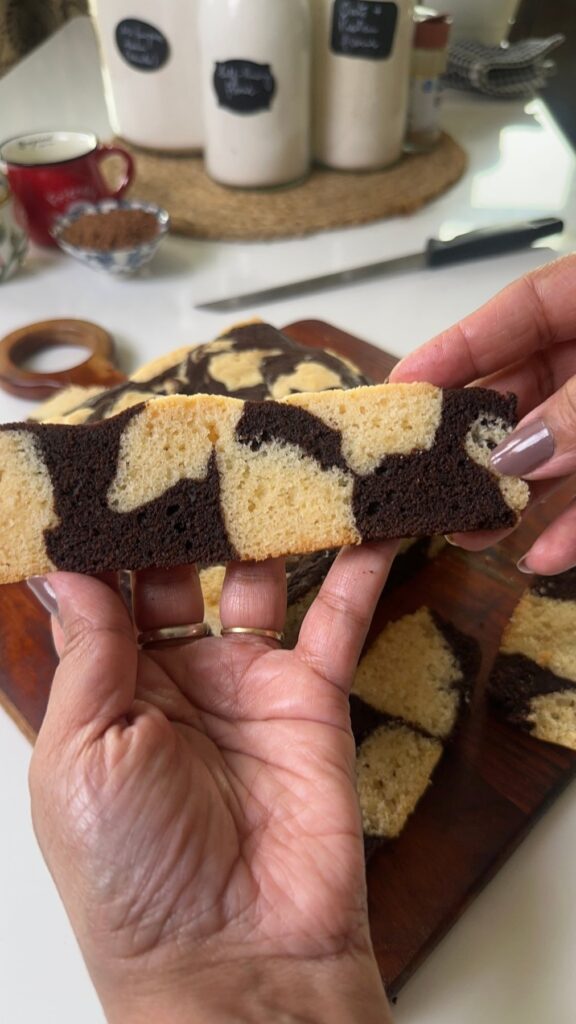 Hand holding a slice of eggless marble butter cake showing the soft crumb