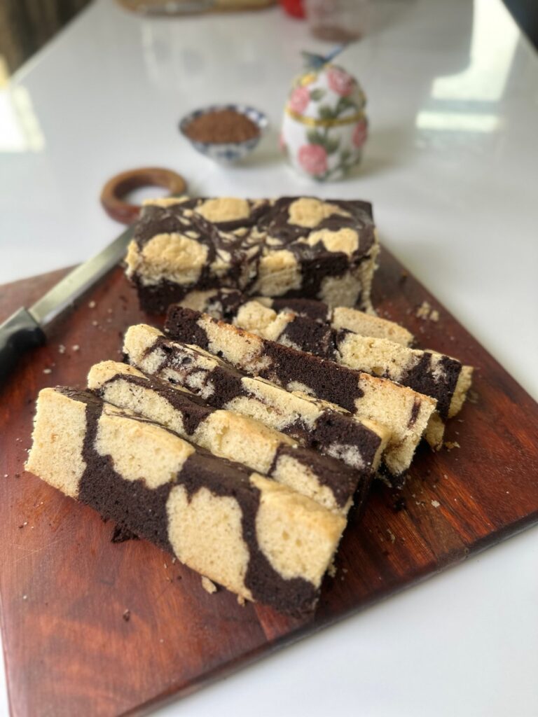 Eggless marble butter cake slices on a board with a rose jar in the background