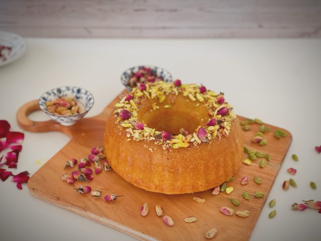 Gulab jamun cake decorated with pistachios and rose petals on a wooden board