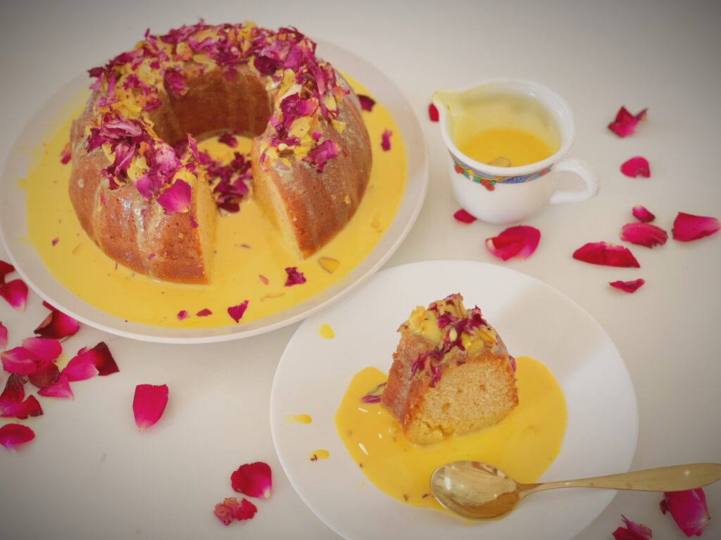 Rasmalai tres leches cake on a plate with rose petals and a bowl of rasmalai milk