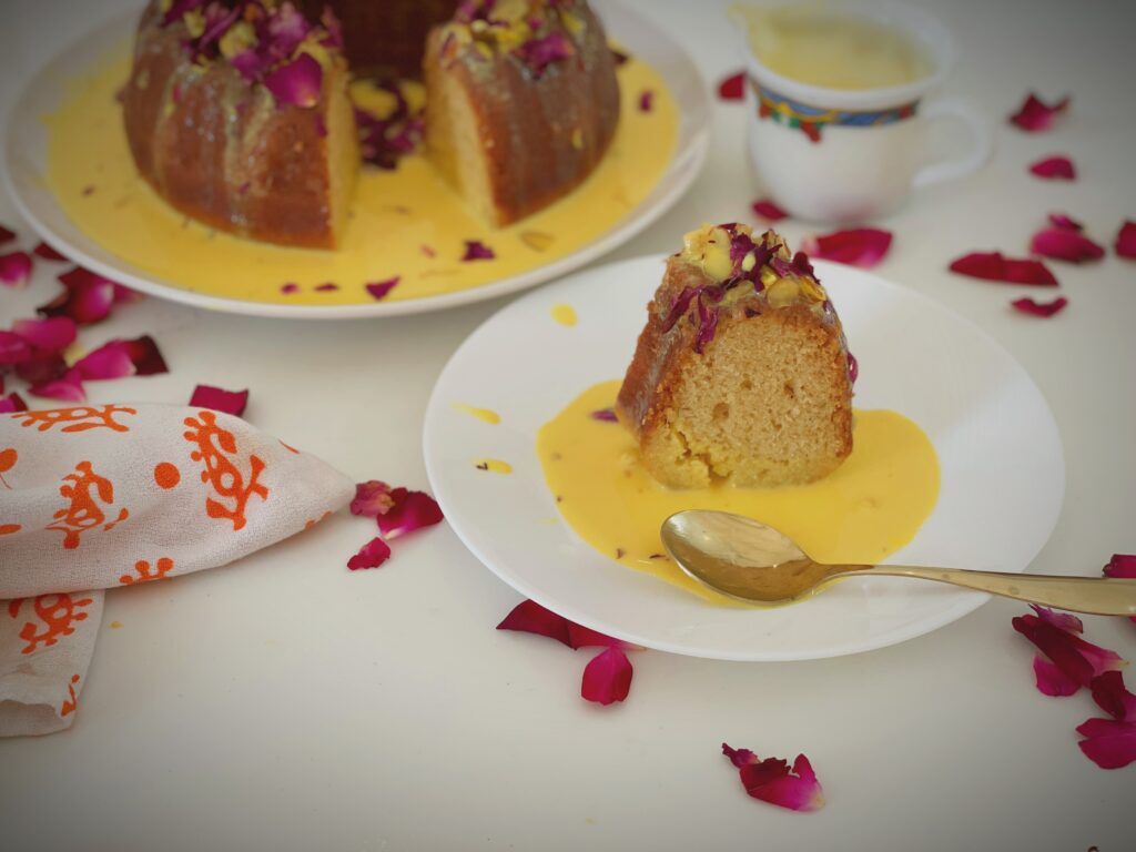 Slice of eggless rasmalai cake in a pool of saffron milk with a spoon