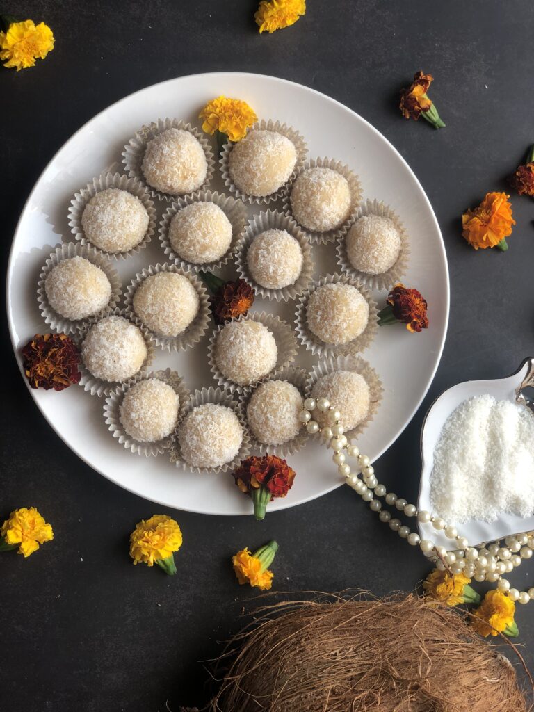 Overhead view of a plate of coconut ladoos with marigolds and fresh coconut