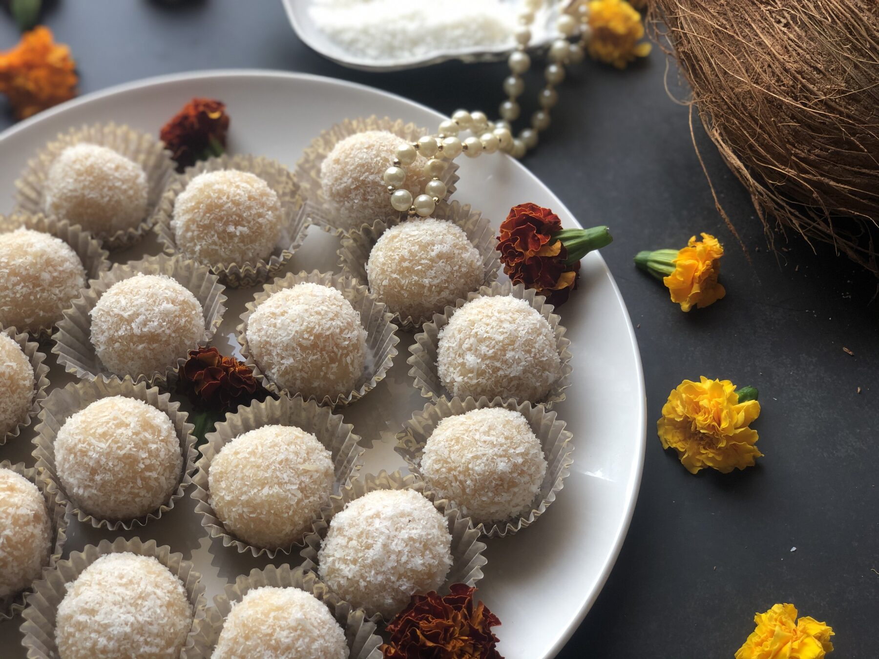 Plate of soft coconut ladoos in paper liners with marigold flowers