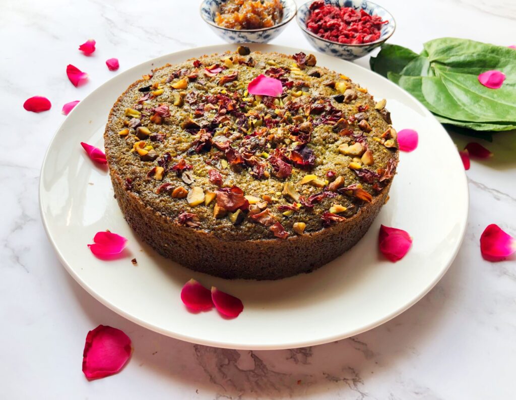Whole eggless paan cake topped with pistachios and rose petals, with betel leaves on the side