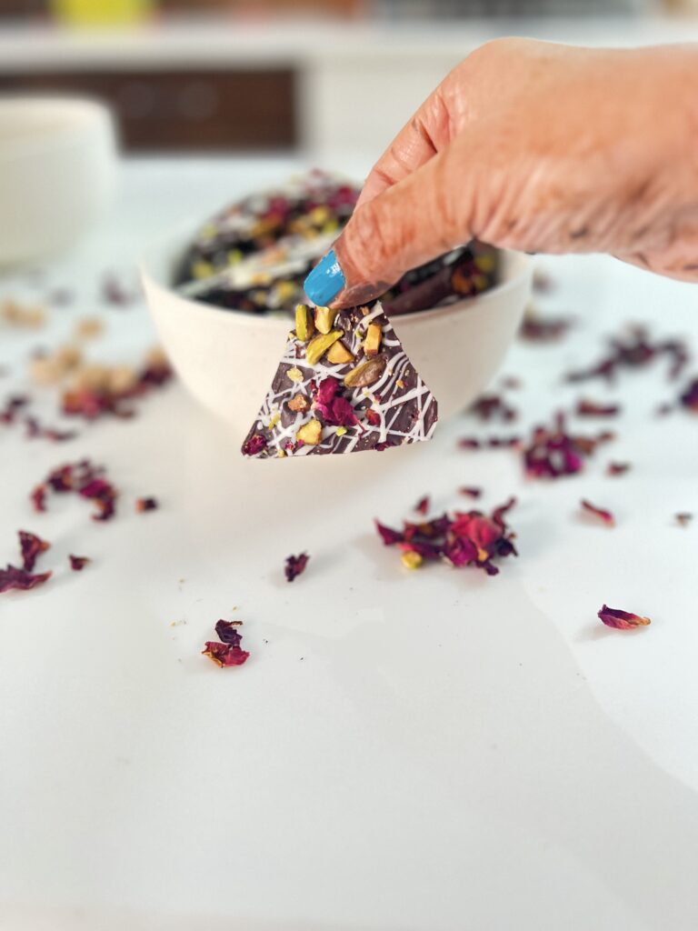 Hand holding a piece of rose pistachio chocolate bark above a bowl