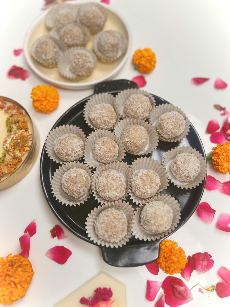 Platter of coconut almond ladoos with a bowl of more ladoos, marigolds and rose petals