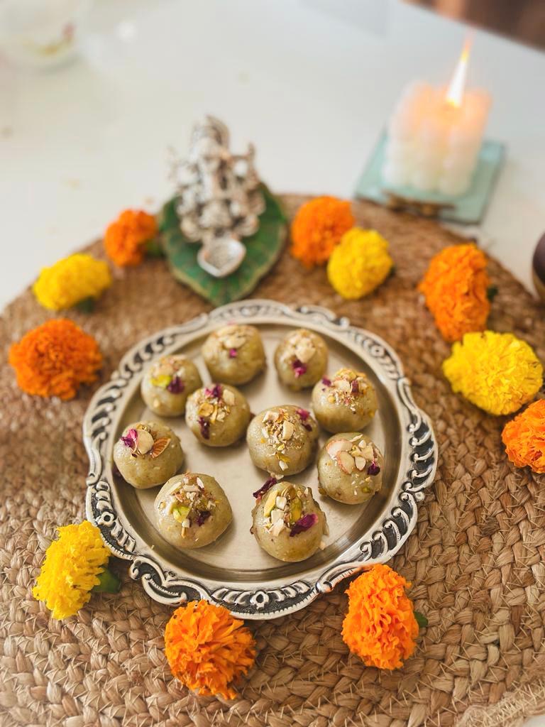 Silver platter of mawa kaju ladoos decorated with pistachios and rose petals, surrounded by marigolds