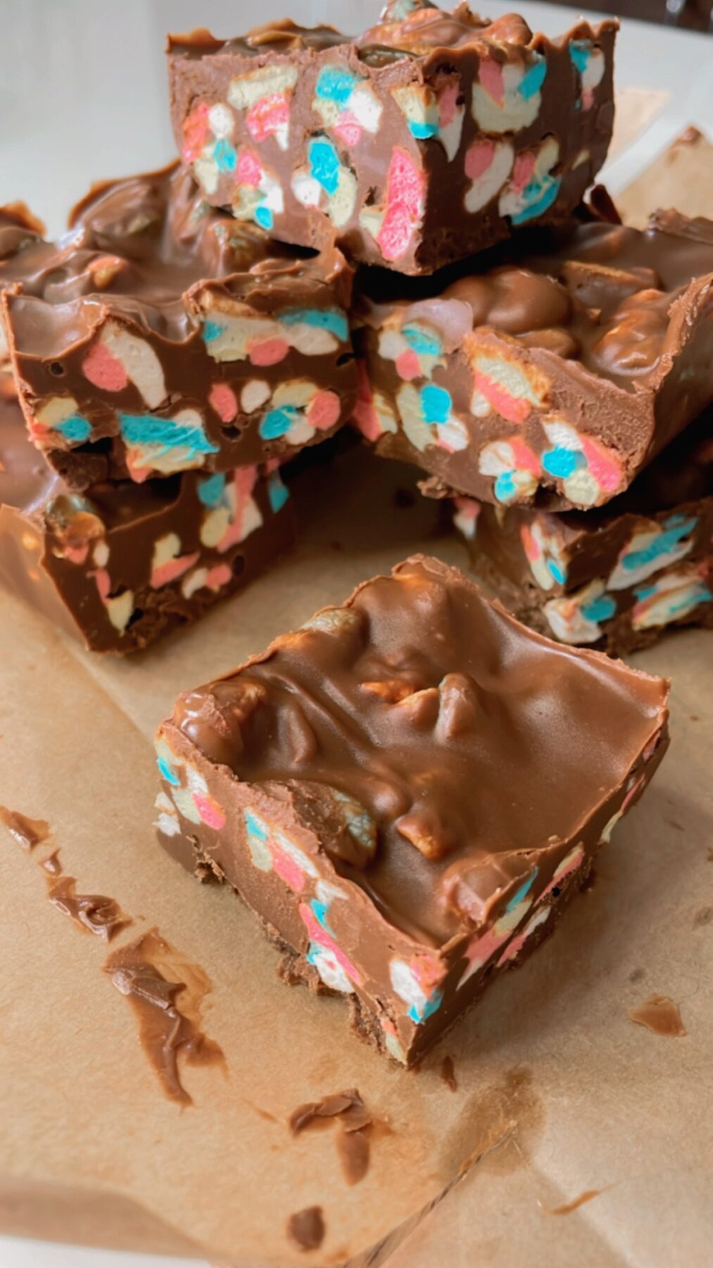 Stack of chocolate marshmallow squares on parchment paper with colourful mini marshmallows inside