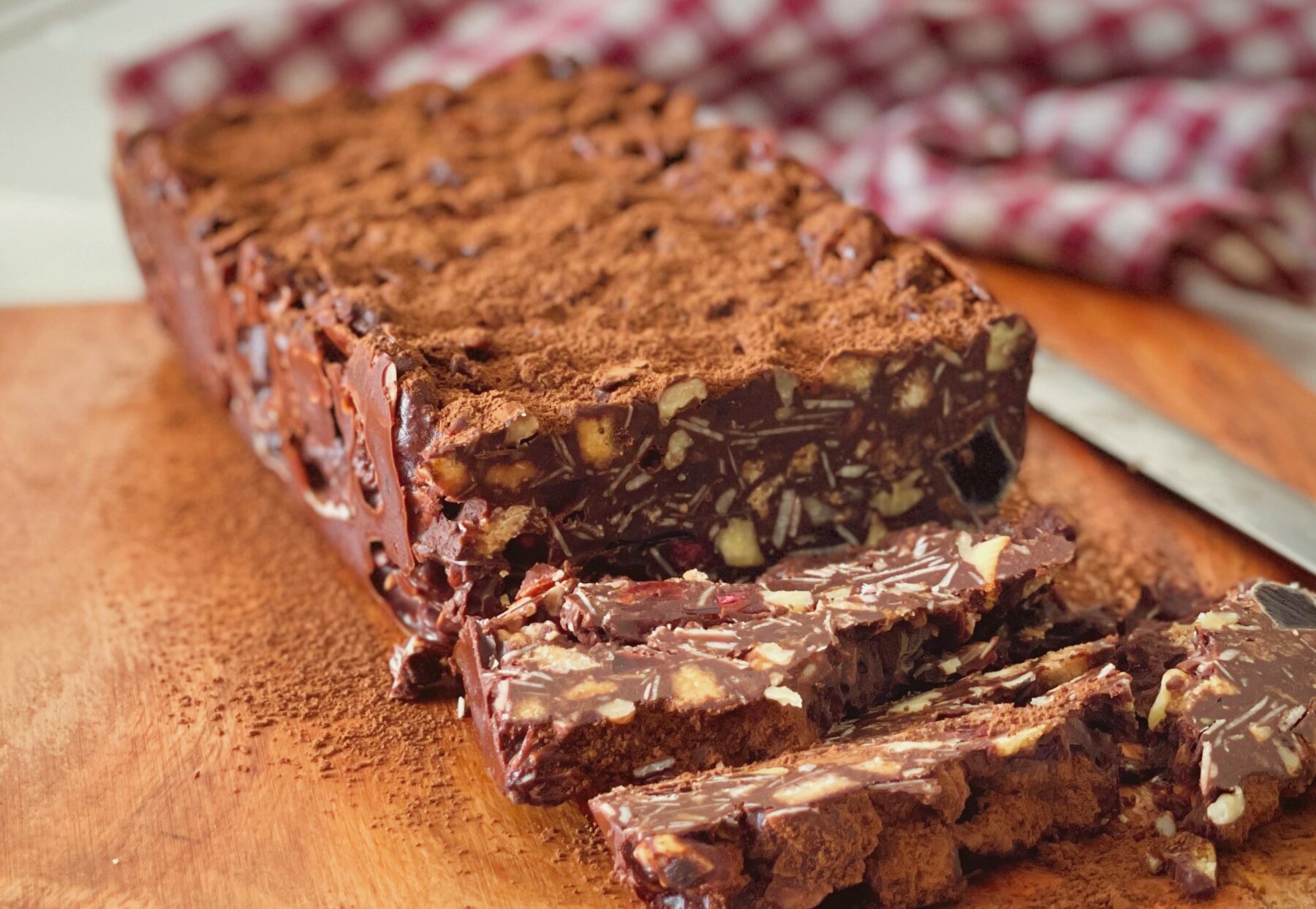 No-bake chocolate biscuit cake dusted with cocoa, sliced to show almonds, walnuts and biscuits inside